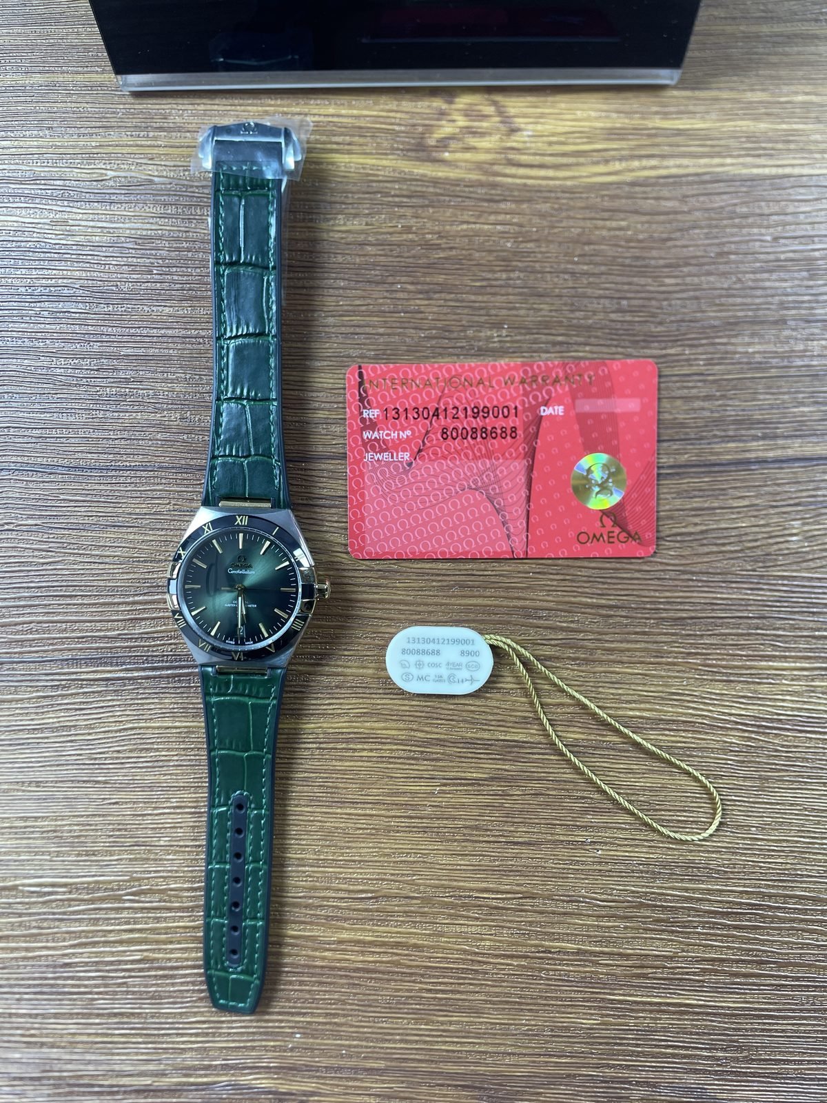 Omega Constellation 131.23.41.21.10.001 replica green dial watch beside mismatched red card and white tag