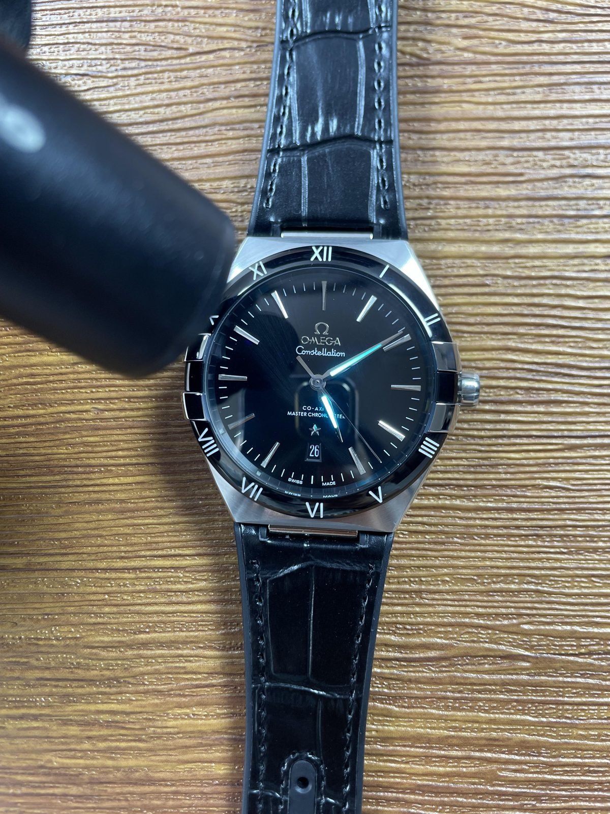 Omega Constellation black dial replica flashlight image showing immediate luminous hand and marker response