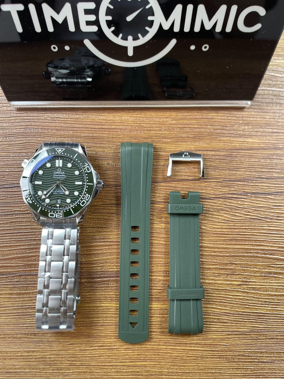 Green dial Seamaster style replica on steel tone bracelet beside detached green grooved strap set and loose hardware