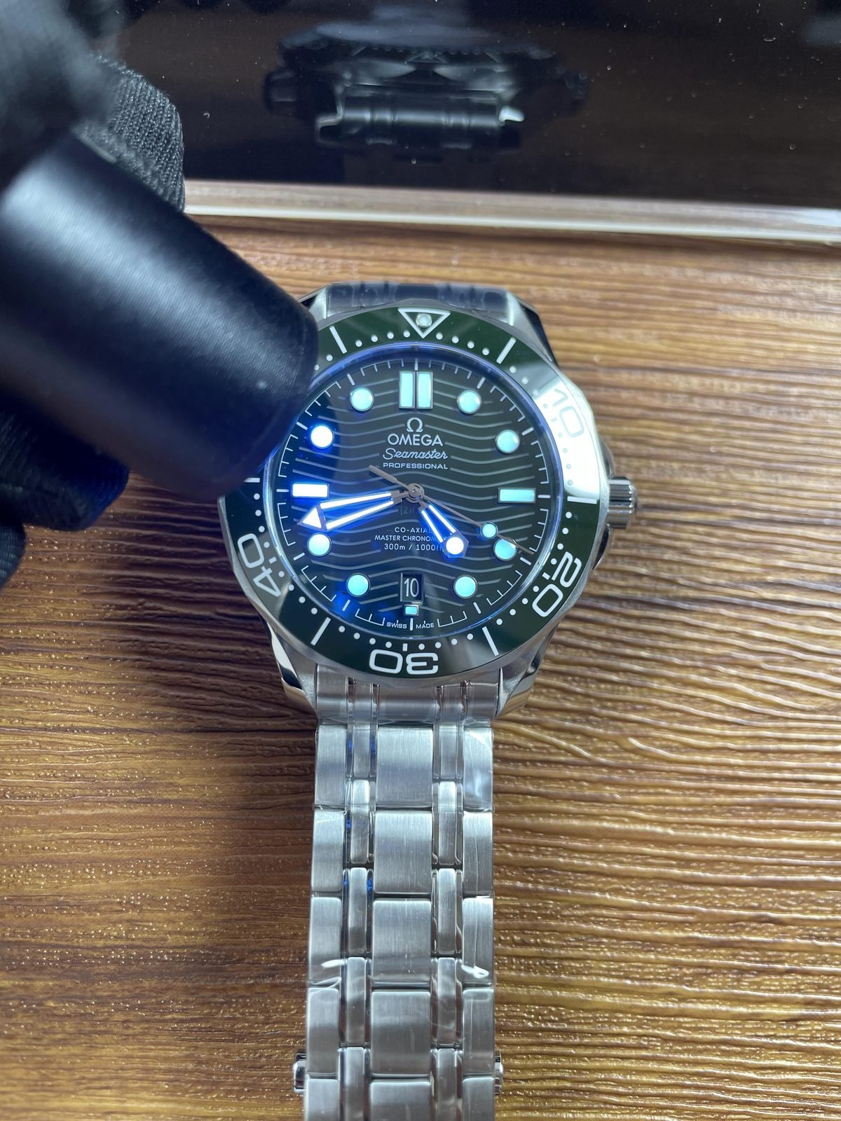 Handheld light producing immediate blue cyan and green luminous style response on green Seamaster style dial