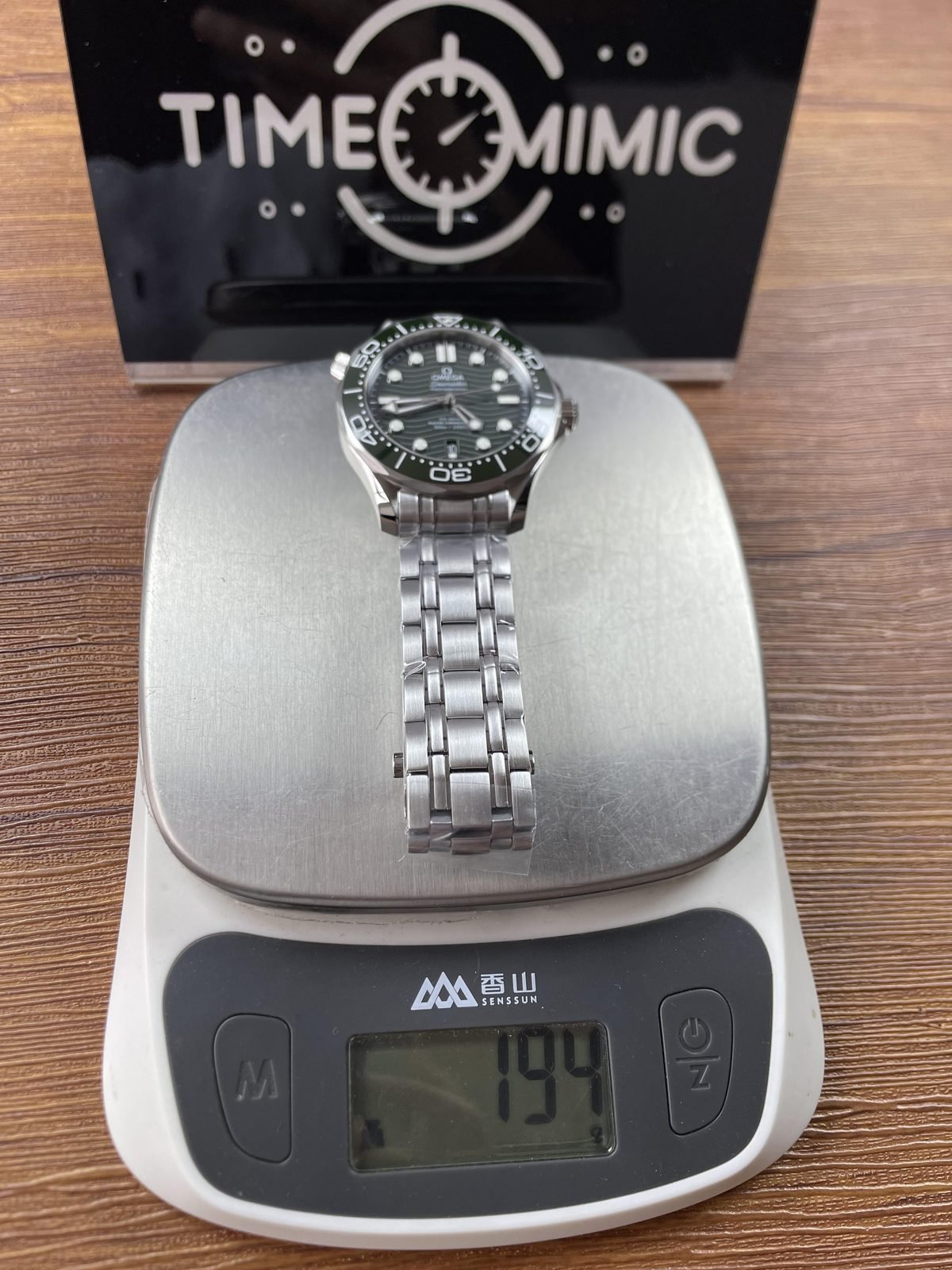 Green Seamaster style replica with filmed steel tone bracelet on scale displaying about 194 grams