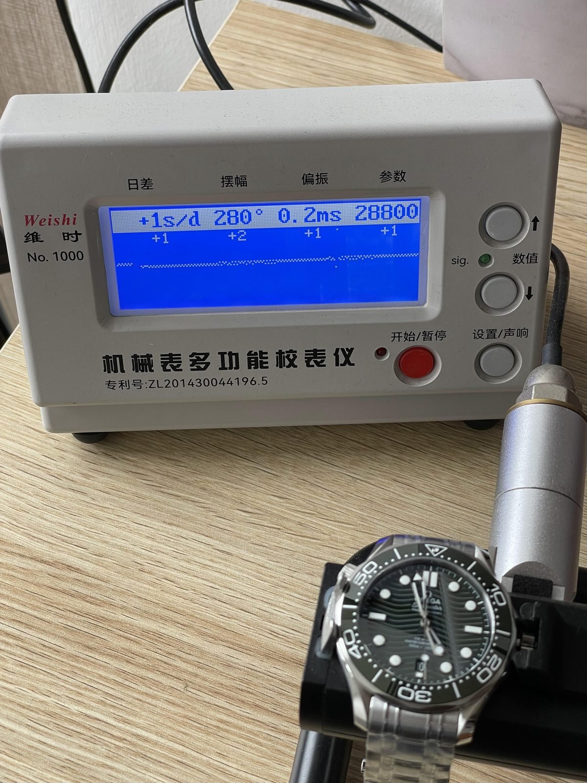 Single timegrapher screen beside green Seamaster style replica showing plus one seconds per day 280 degrees 0.2 milliseconds and 28800