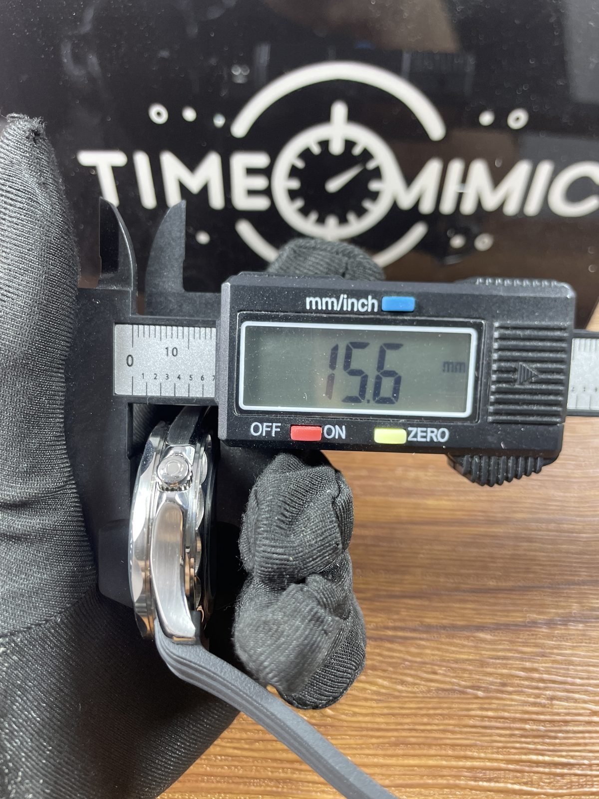 Digital calliper displaying about 15.6 millimetres along thickness direction of black Seamaster style replica