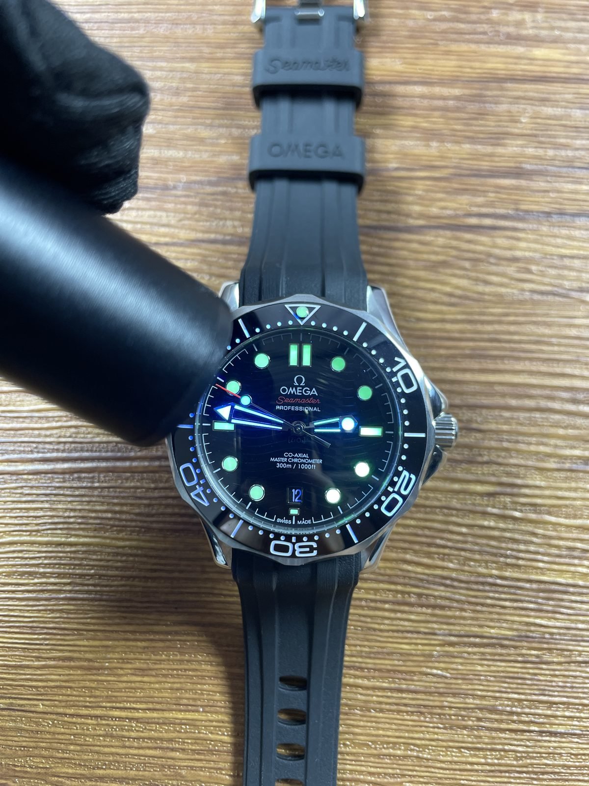 Handheld light producing immediate green and blue luminous style response on black Seamaster style dial