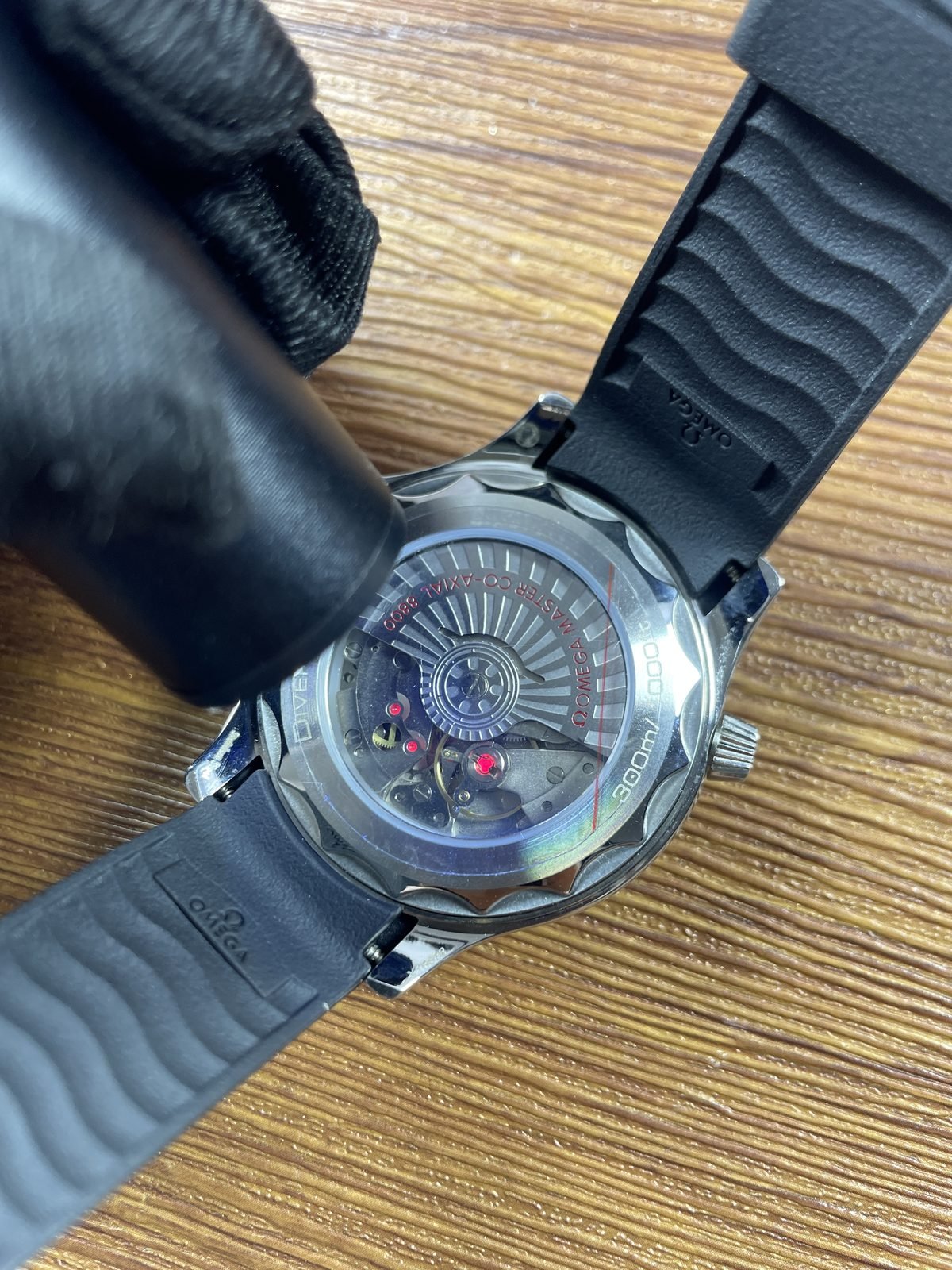 Close transparent caseback view of decorated automatic looking movement and balance area in black Seamaster style replica