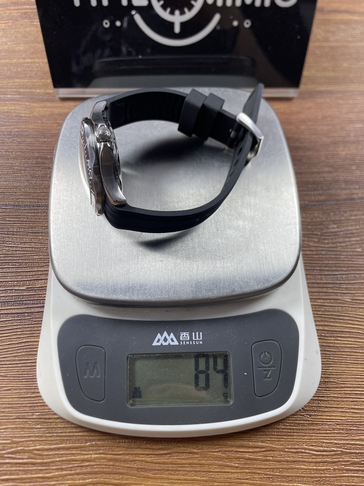 Black strap Seamaster style replica on scale displaying approximately 84 grams