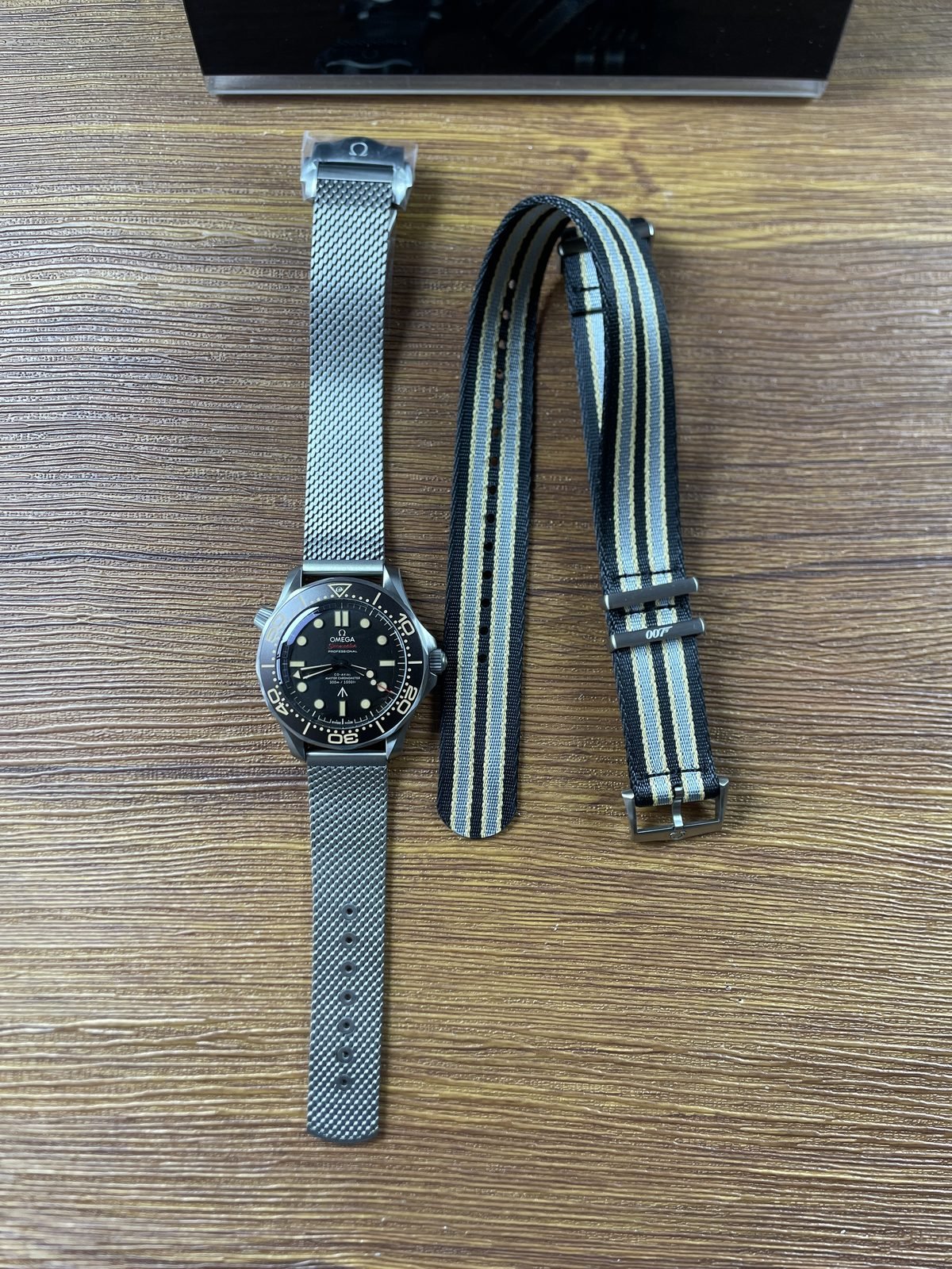 No-date dark tropical tone Omega Seamaster 210.90.42.20.01.001 style replica on mesh bracelet beside striped woven strap