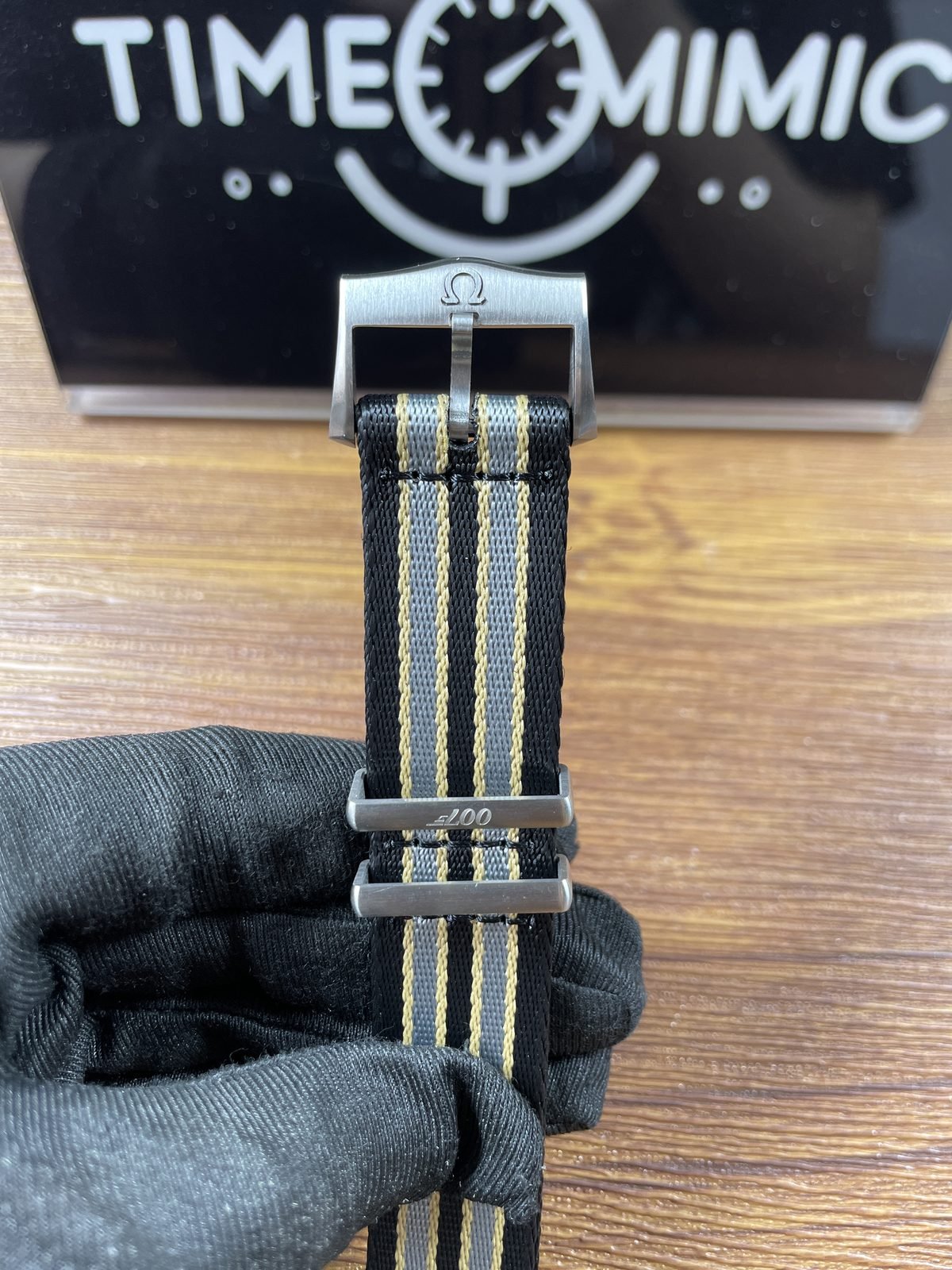 Close view of striped woven pass-through strap pin buckle Omega style symbol twin keepers and 007 style mark
