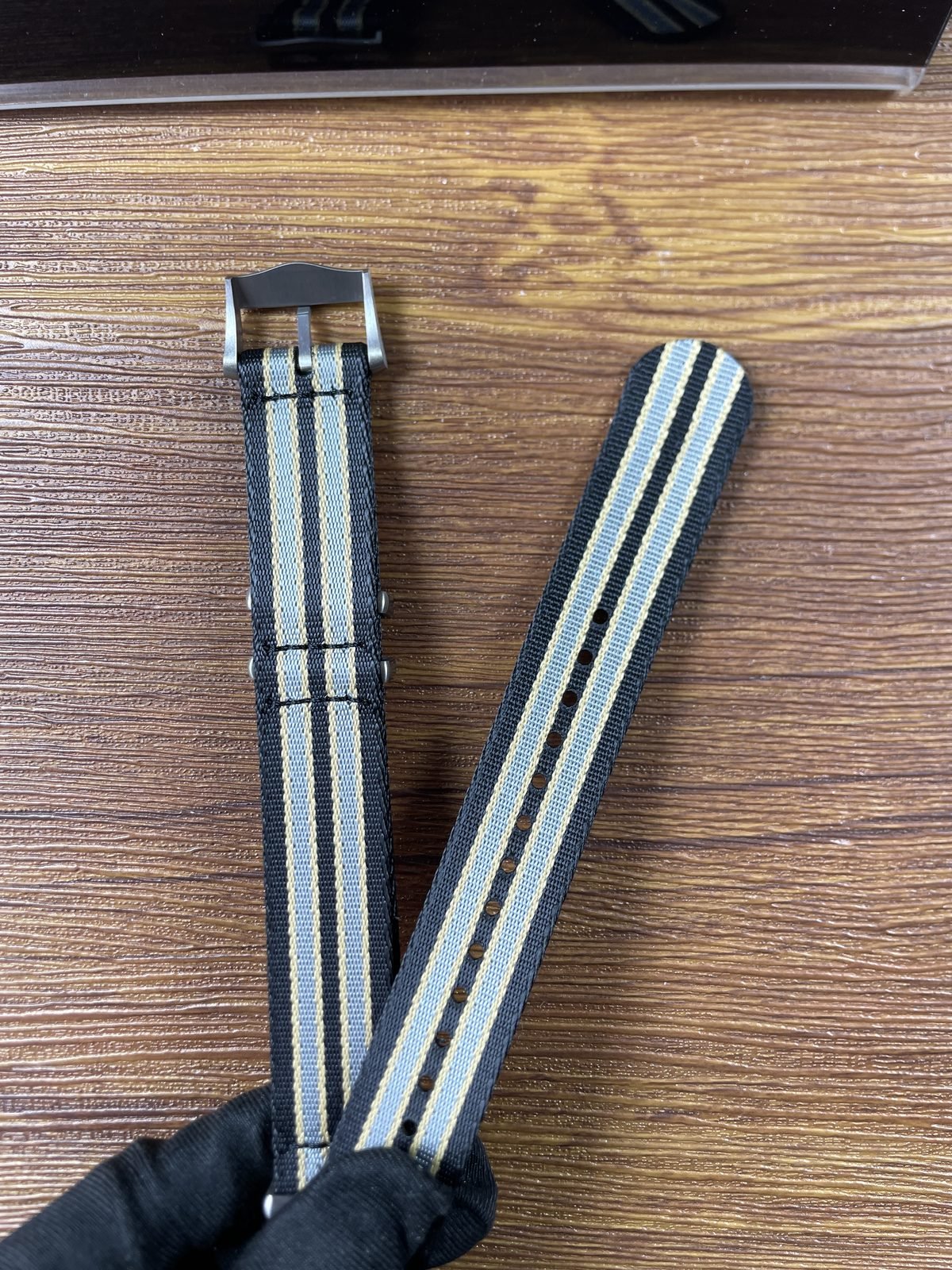 Two ends of black grey beige striped woven strap showing holes stitching buckle and keepers