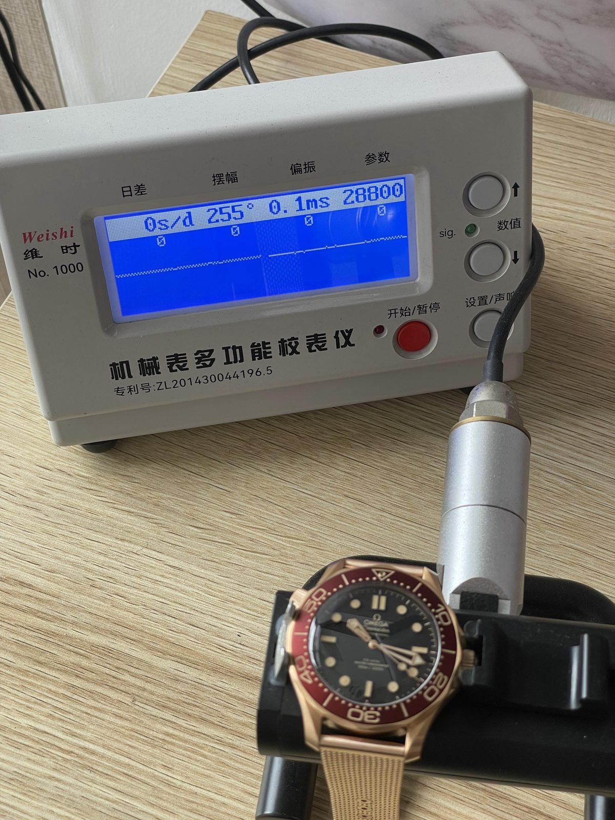 Single timegrapher screen beside warm tone Seamaster replica showing zero seconds per day 255 degrees 0.1 milliseconds and 28800