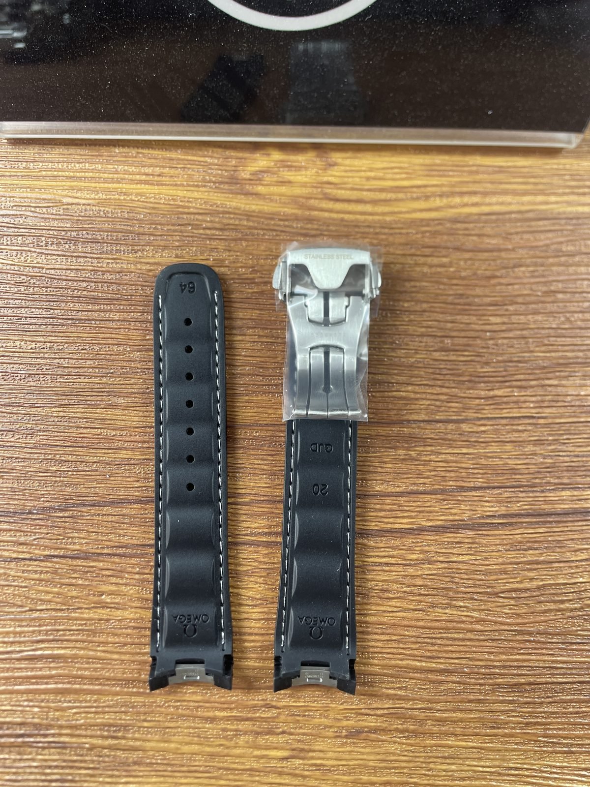 Undersides of loose black strap pieces with 64 20 QJB Omega and stainless steel style markings