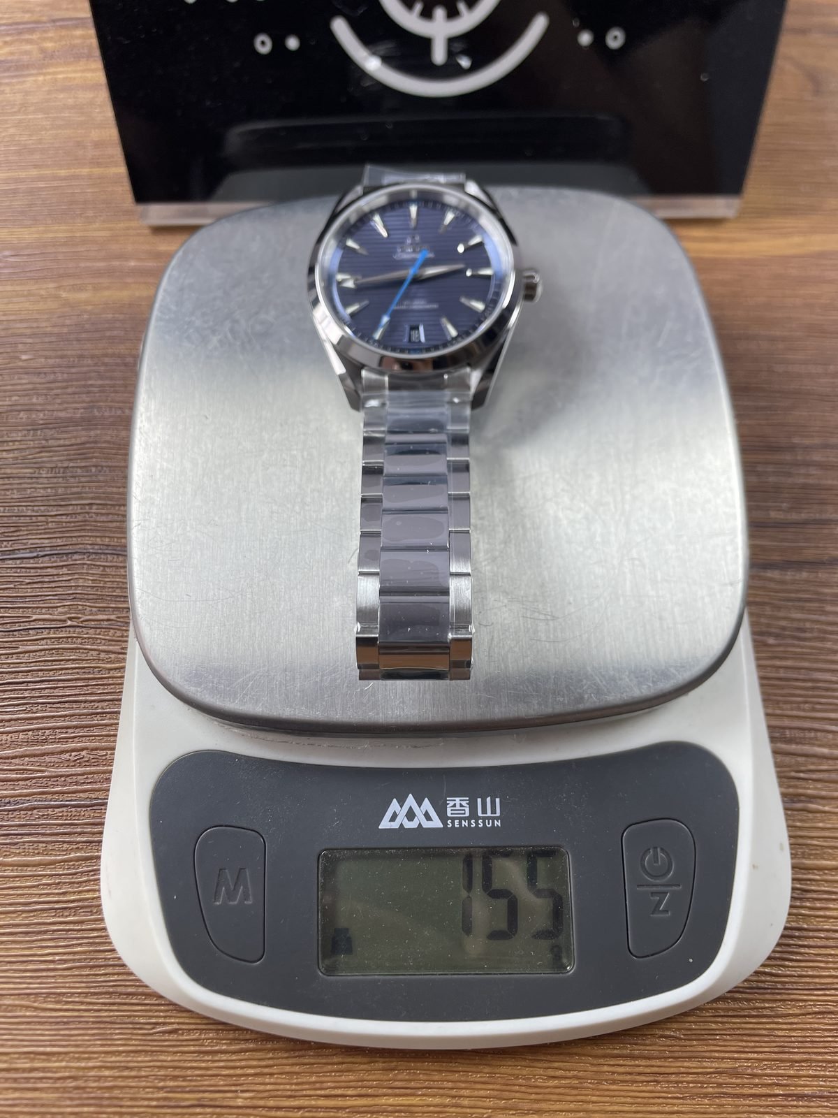 Blue horizontal stripe Aqua Terra replica on digital scale displaying about 155 grams